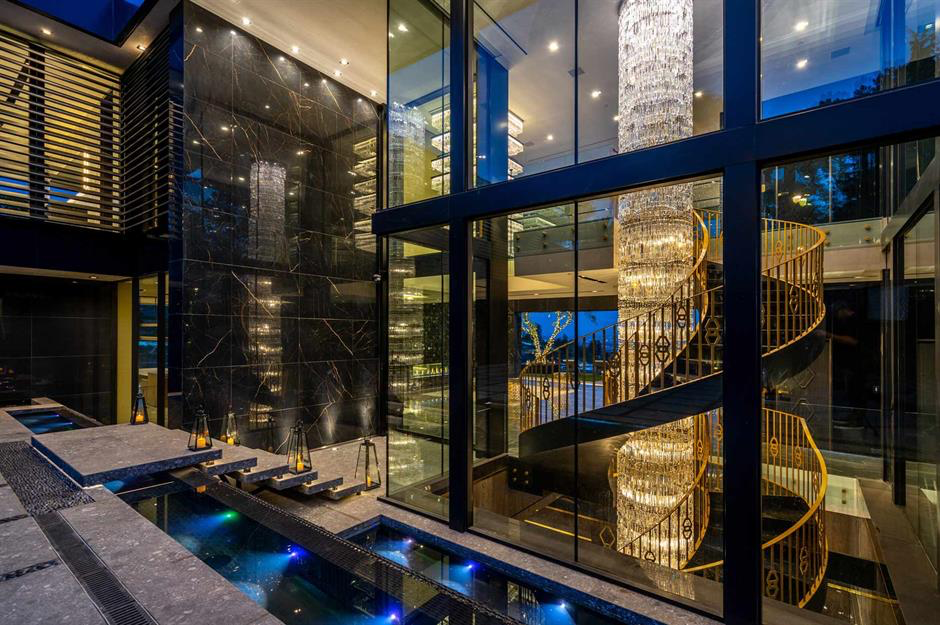 A dramatic glass-walled great room with a spiral staircase and crystal chandelier